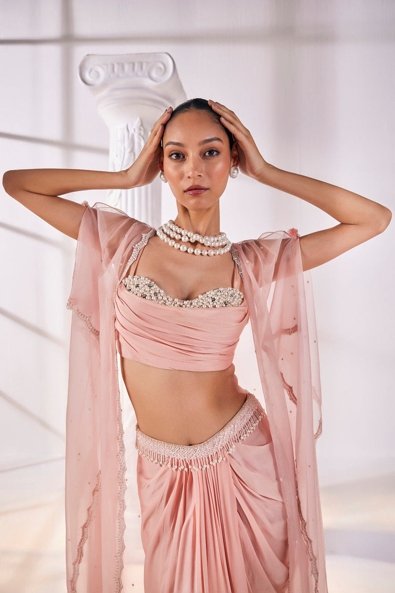 Peach Draped Skirt In Satin Georgette Paired With A Belt And A Pearl Detailed Blouse With A Soft Organza Cape.